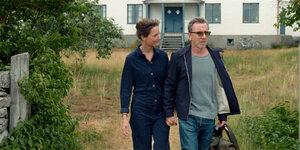 Die beiden Schauspieler Vicky Krieps und Tim Roth auf dem Land vor einem weißen Sommerhaus