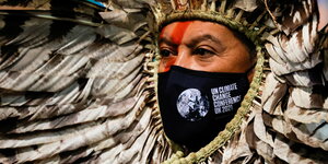 Indigener mit Gesichtsmaske und Federschmuck