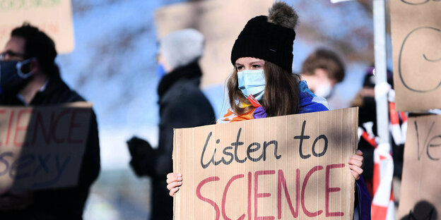 Eine Frau trägt ein Schild "listen to science"