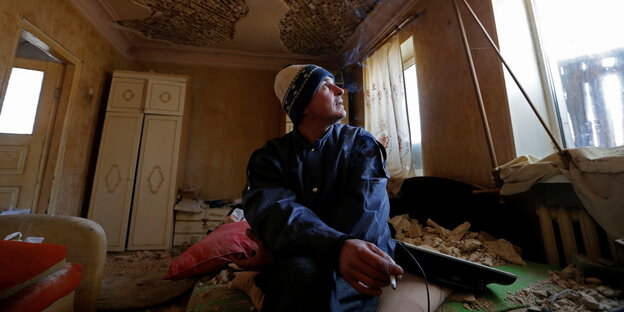 Ein Mann sitzt in den Trümmern seines Hauses und raucht