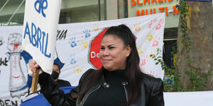 Eine junge Frau mit schwarzen Haaren lächelt und hält ein Demo-Schild mit der Aufschrift "Heroes de Abril", April-Helden
