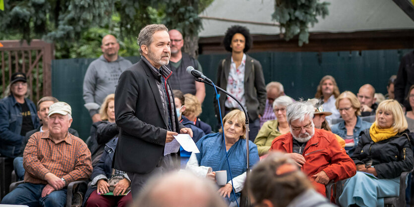 Sören Benn steht inmitten einer Gruppe von Menschen am Mikrofon