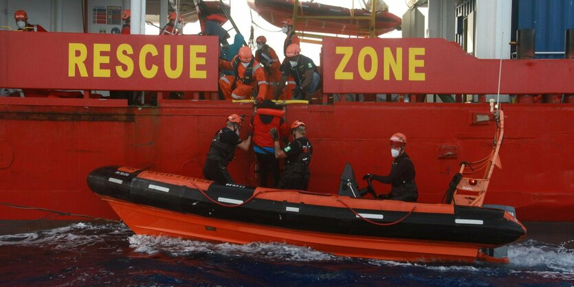 Menschen steigen von einem Schlauchboot auf eine größeres Schiff um.