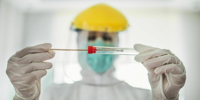 Ärztin in Schutzkleidung mit Teststäbchen in der Hand