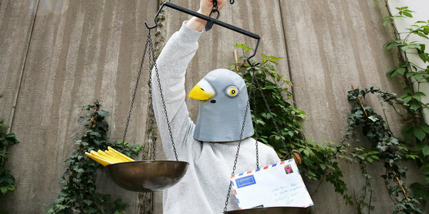 Ein Mensch mit Vogelmaske hält eine Waage mit Briefen
