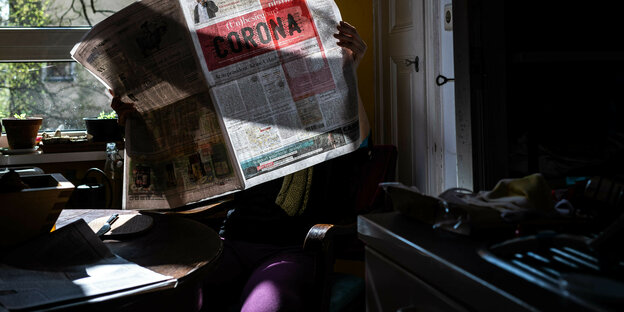 Ein Mensch liest den Tagesspiegel, der auf der Titelseite groß Corona stehen hat, in der Küche.