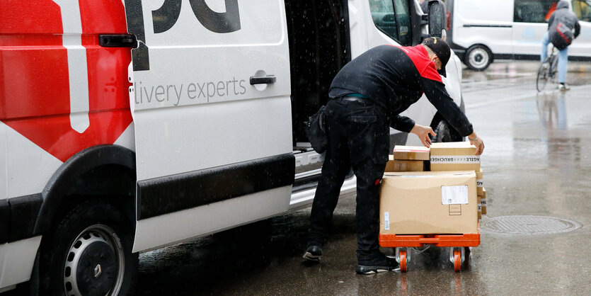 Paketzusteller verlädt Pakete auf eine Karre.