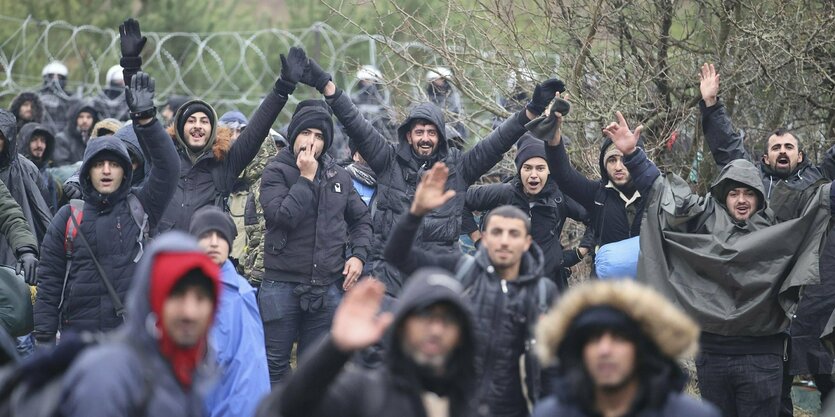 Menschen it erhobener Hand, dafinter Stacheldraht