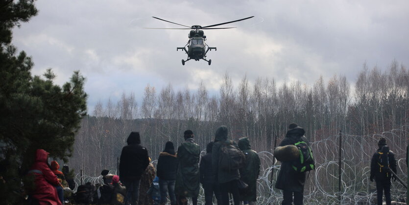 Ein Hubschrauber über Menschen an einen Stacheldrahtzaun.