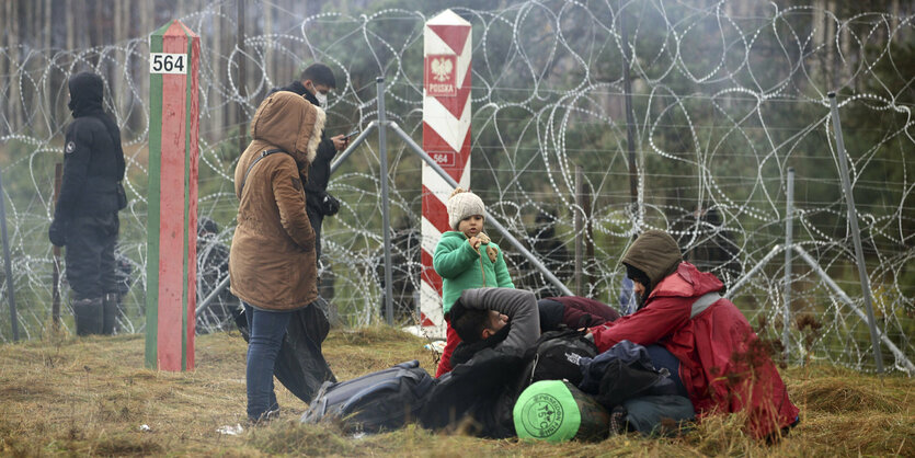 Kinder und Erwachsene, Geflüchtete, an der belarusisch-polnischen Grenze vor Stacheldraht