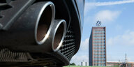 Auspuffrohr eines VW, dahinter das Hochhaus mit dem VW-Emblem in Wolfsburg