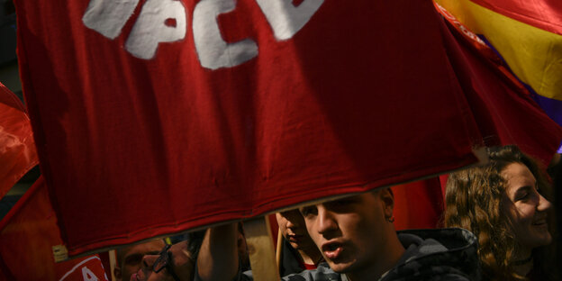 Große rote Fahne mit dem Logo der PCE, die von jungen Leuten gehalten wird