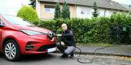 Alexander Köhl kniet mit einem Elektrokabel vor seinem roten Auto, das vor einem Einfamilienhaus parkt