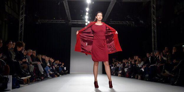 Frau mit rotem Mantel bei einer Modenschau.