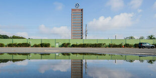 das VW-Hochhaus in Wolfsburg spiegelt sich in einer Pfütze auf dem Mitarbeiterparkplatz