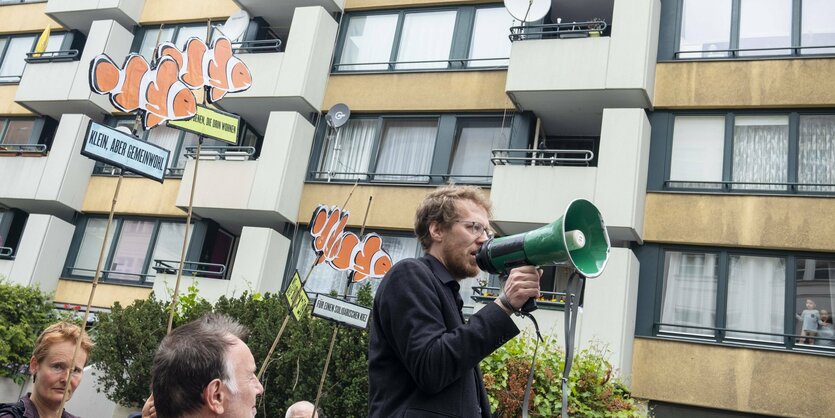 Ein Mann steht mit einem Megaphon vor einer Häuserwand