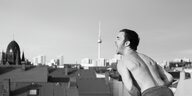 Albrecht Schuch als Thomas Brasch steht mit nacktem Oberkörper auf einem Dach, den Berliner Fernsehturm im Hintergrund.