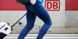 Eine Person läuft an einem Bahnsteig an einem Zug der deutschen bahnmit einem Koffer vorbei
