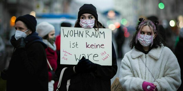 Frauenb mit Gesichtsmaske, in Winterkleidung protestieren mit einem Schild: Wohnraum ist keine Ware