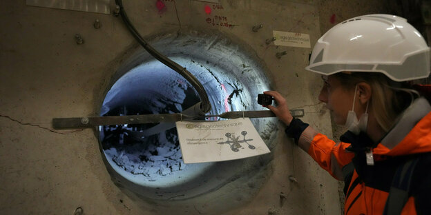 Eine frau mit Schutzkleidung und Helm beobachtet Radioakticen Müll in einem unterirdischen Labor