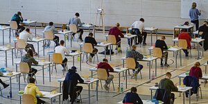 Schüler sitzen an Tischen in einer Turnhalle und schreiben eine Prüfung.