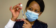 Eine Frau mit Maske mit einer Impfspritze.