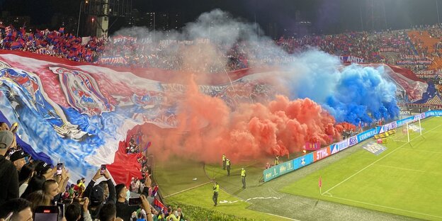 Blau und rote Pyroschwaden in der Stadionkurve