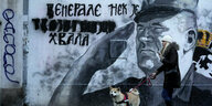 eine Frau geht mit ihrem Hund an einem Wandgemälde mit einem salutierenden Kiregsverbrecher Ratko Mladic vorbei