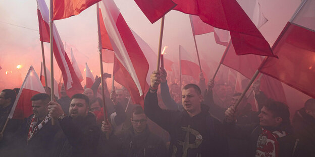 Teilnehmer des Marsches in Warschau schwingen rot-weiße Fahnen durch die rauchige Luft