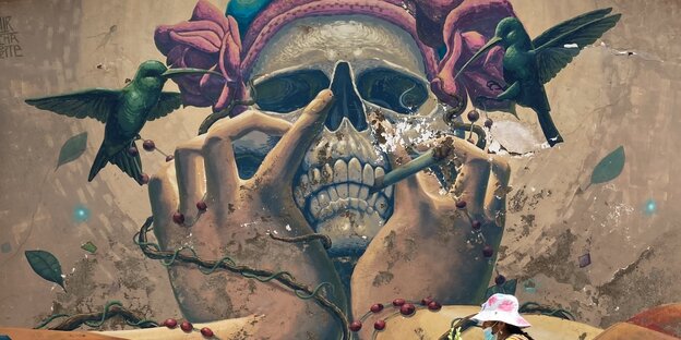 Ein Wandgemälde zeigt einen Totenkopf, der eine Zigarette im Mund hat, umschwirrt von Kolibris