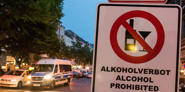Straßenszene mit Alkoholverbotsschild und Polizeiauto im Hintergrund