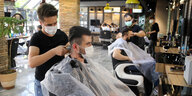 Ein Friseur schneidet einem Kunden die Haare mit Maschiene. Beide tragen Maske.