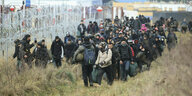 Flüchtlinge gehen an einem Stacheldrahtzaun an der belarussisch-polnischen Grenze entlang