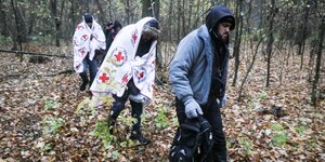 Drei Männer, davon zwei in Decken vom Roten Kreuz gehüllt, an der polnisch-belarusischen Grenze