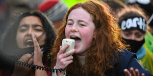 Drei Mädchen auf einer Demo rufen laut und sehen aufgeregt aus, eine hält die Hand an den Mund um lauter zu sein, eine andere ruft inbrünstig in ein Megafon