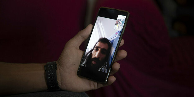 Auf einem Handybildschirm ist das Gesicht eines hageren, bärtigen Mannes zu sehen