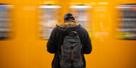 Ein Mann mit Rucksack auf dem Rücken steht vor einer fahrenden Bahn