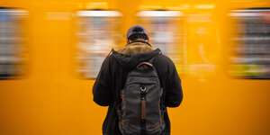 Ein Mann mit Rucksack auf dem Rücken steht vor einer fahrenden Bahn