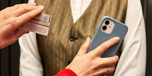 Eine Person zeigt einen Personalausweis und eine Smartphone.