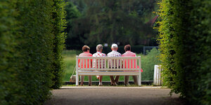 Mehrere ältere Personen sitzen auf einer Parkbank im Schlosspark Pillnitz in Sachsen.