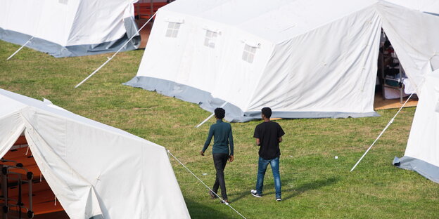 Zwei Flüchtlinge laufen zwischen Zelten entlang.