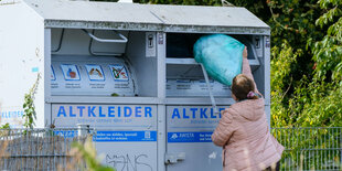 eine Frau wirft einen blauen Sack in einen Altkleidercontainer