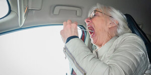 Eine aeltere Frau in einem Auto reisst ihren Mund auf, um ein Stäbchen hinein zu stecken