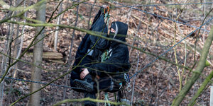 Ein Aktivist sitzt im Wald auf einem Seil zwischen Bäumen