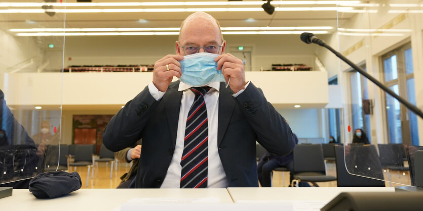 Ein Mann mit Brille im Gericht setzt sich einen Mund-Nasen-Schutz auf