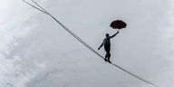 Eine Person balanciert mit einem Schirm auf einem Seil.