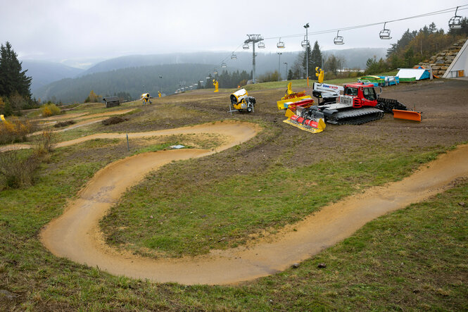 Pistenbully und Schneekanonen stehen am Lift bereit, eine neblige Herbstlandschaft mit Bergen