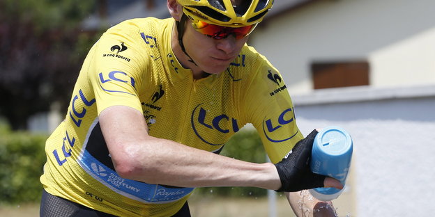 Tour de France-Fahrer Christ Froome im gelben Trikot. Er sitzt auf einem Fahrrad und spritzt sich mit einer Flasche Wasser ab.