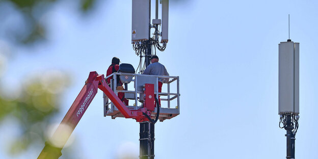 Arbeiter installieren auf einem Dach Mobilfunkmasten.
