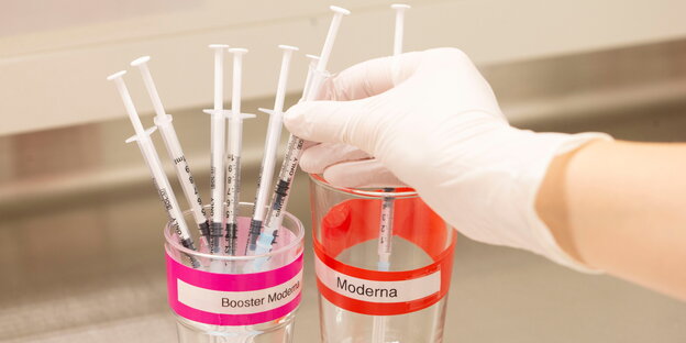 Becher mit Impfspritzen in einem Glas mit der Aufschrift Booster Moderna